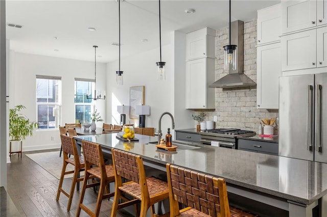 kitchen featuring pendant lighting, white cabinetry, sink, stainless steel appliances, and wall chimney range hood