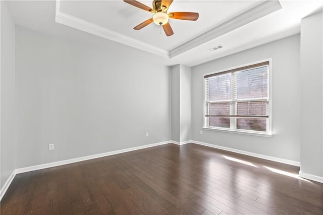 empty room with a tray ceiling, dark hardwood / wood-style floors, and ornamental molding