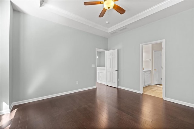 unfurnished bedroom featuring a tray ceiling, ceiling fan, crown molding, connected bathroom, and dark hardwood / wood-style floors