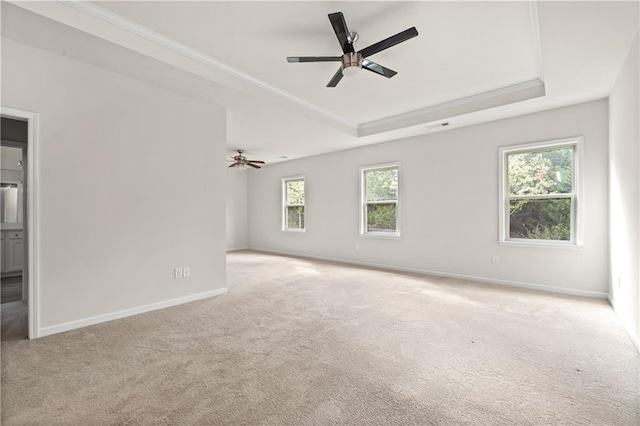 empty room with a raised ceiling, ceiling fan, plenty of natural light, and light colored carpet