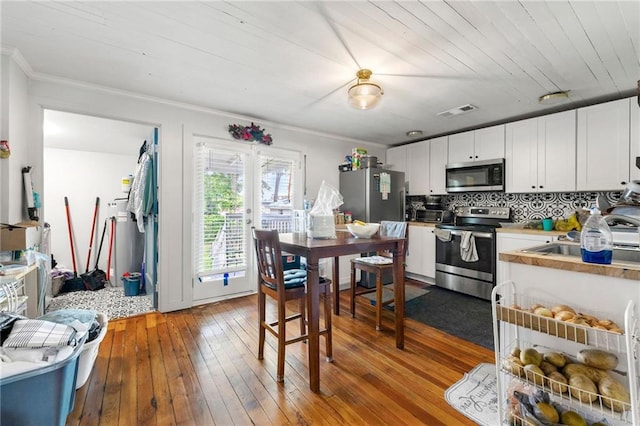 5150 Wheat St NE, Covington, GA 30014 - kitchen with stainless steel appliances, wood-type flooring, tasteful backsplash, white cabinetry, and crown molding