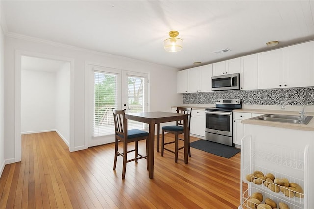 5150 Wheat St NE, Covington, GA 30014 - kitchen with stainless steel appliances, a sink, light wood-style floors, decorative backsplash, and crown molding