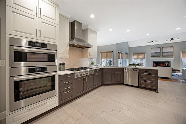 kitchen featuring tasteful backsplash, light countertops, appliances with stainless steel finishes, wall chimney exhaust hood, and a sink