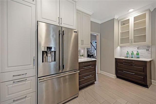 kitchen featuring high end fridge, ornamental molding, tasteful backsplash, light countertops, and glass insert cabinets