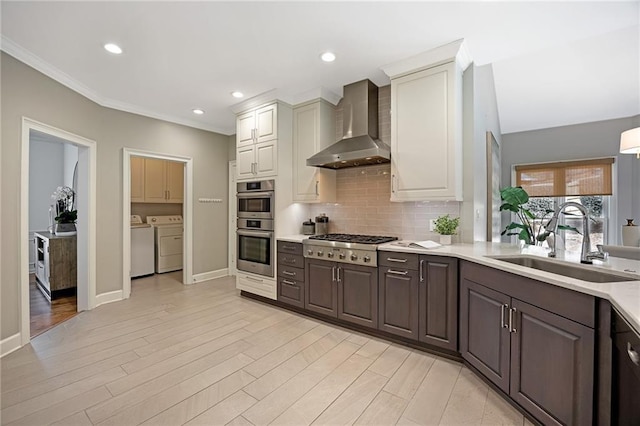 kitchen with washer and clothes dryer, light countertops, stainless steel appliances, wall chimney exhaust hood, and a sink