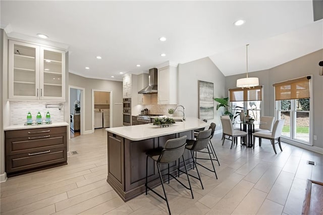 kitchen featuring washer and clothes dryer, a peninsula, a breakfast bar area, wall chimney exhaust hood, and light countertops