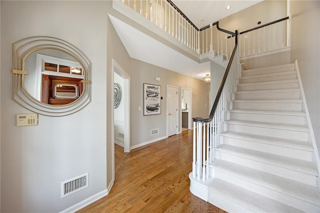 stairway with visible vents, baseboards, a towering ceiling, and wood finished floors