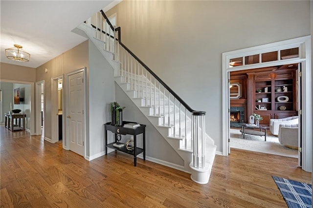 stairway with an inviting chandelier, a fireplace, baseboards, and wood finished floors