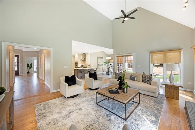 living room with ceiling fan, light wood-type flooring, baseboards, and vaulted ceiling