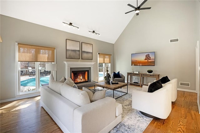 living area featuring visible vents, a healthy amount of sunlight, a warm lit fireplace, and wood finished floors