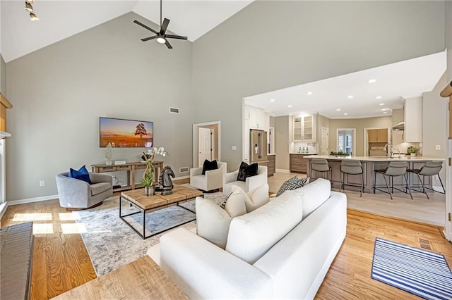 living room with recessed lighting, high vaulted ceiling, light wood-type flooring, and baseboards