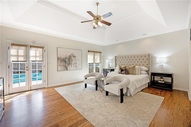 bedroom with a tray ceiling, access to outside, wood finished floors, and french doors