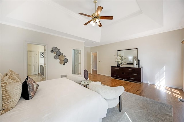 bedroom featuring visible vents, crown molding, baseboards, a tray ceiling, and wood finished floors