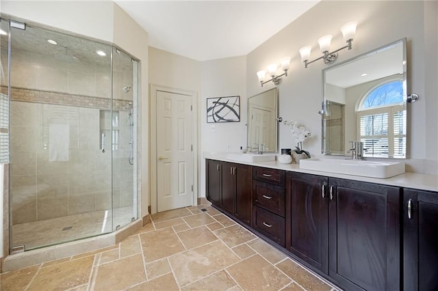 bathroom with a sink, a stall shower, stone tile flooring, and double vanity