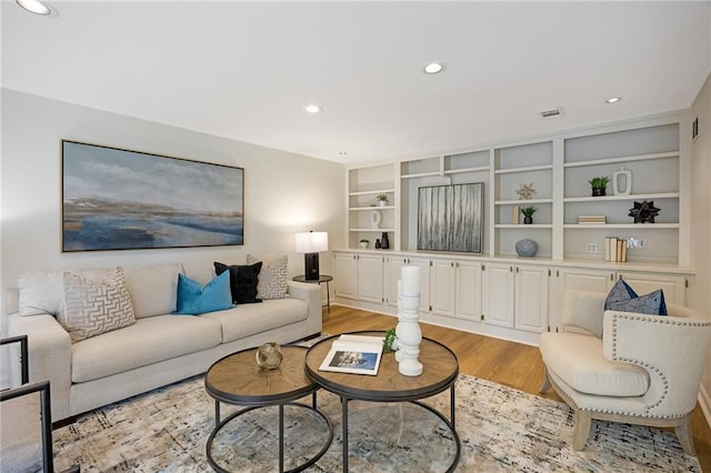 living room featuring visible vents, built in shelves, recessed lighting, and light wood-type flooring