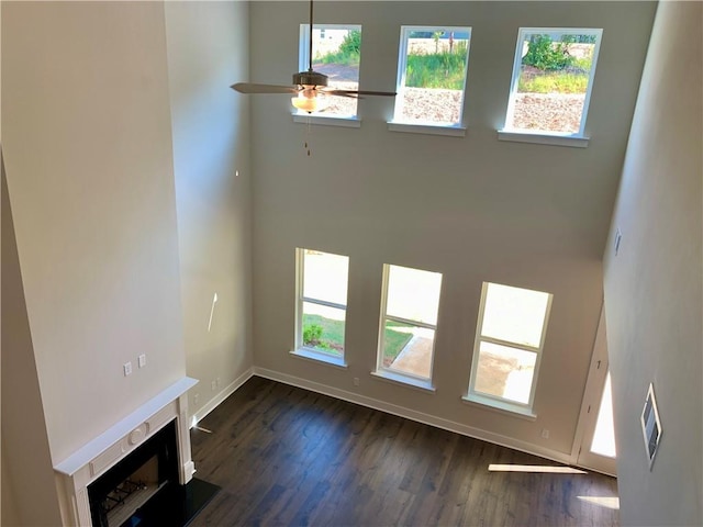 unfurnished living room featuring ceiling fan, a high ceiling, dark hardwood / wood-style flooring, and a wealth of natural light