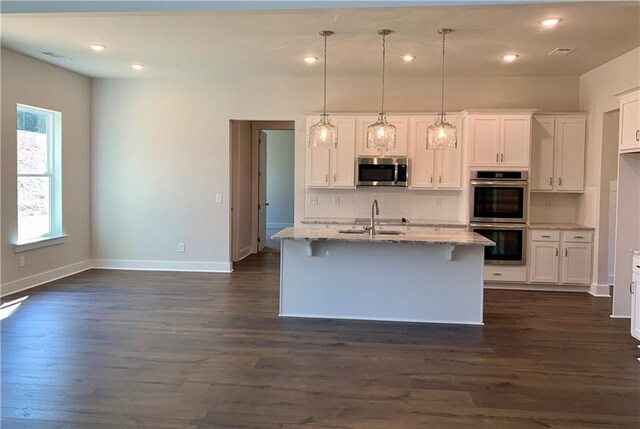 kitchen with appliances with stainless steel finishes, white cabinetry, light stone counters, dark hardwood / wood-style flooring, and a kitchen island with sink