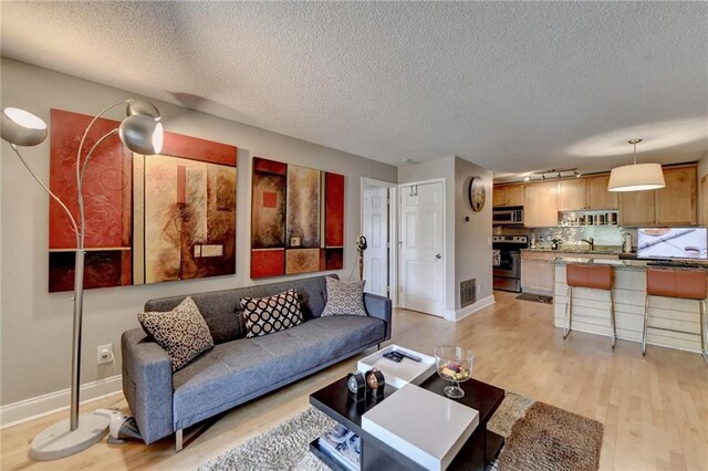 living room with sink, a textured ceiling, and light hardwood / wood-style flooring