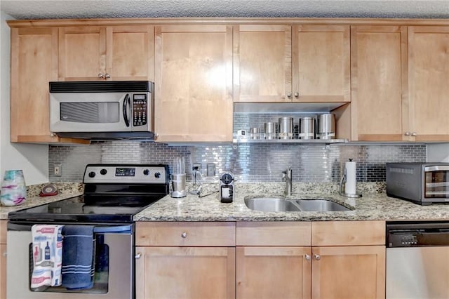 kitchen with appliances with stainless steel finishes, a sink, light stone counters, and tasteful backsplash