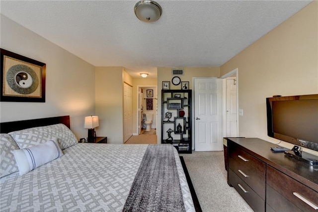 bedroom with a textured ceiling, connected bathroom, visible vents, and light colored carpet