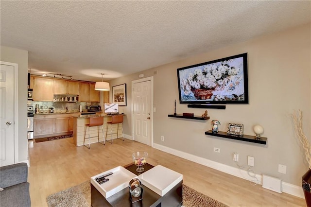 living room featuring light wood-type flooring, track lighting, baseboards, and a textured ceiling