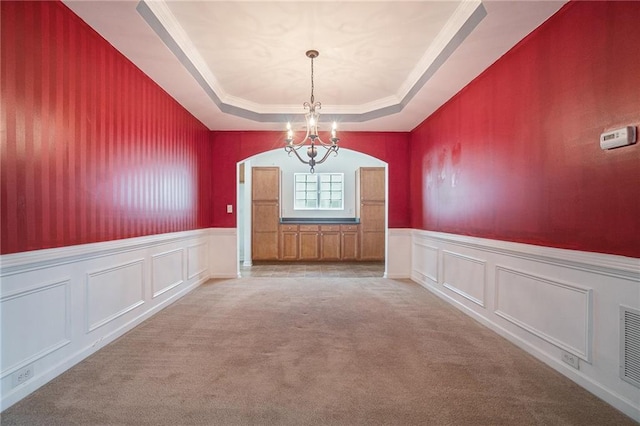 7761 Parkside Dr, Lithia Springs, GA 30122 - unfurnished dining area with a chandelier, a tray ceiling, light colored carpet, wainscoting, and a decorative wall