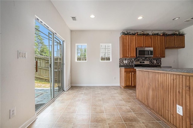 7761 Parkside Dr, Lithia Springs, GA 30122 - kitchen featuring stainless steel microwave, dark countertops, recessed lighting, brown cabinets, and backsplash