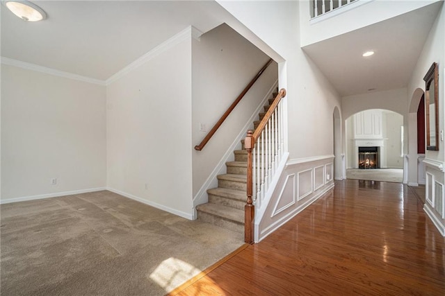 7761 Parkside Dr, Lithia Springs, GA 30122 - staircase with a lit fireplace, ornamental molding, arched walkways, baseboards, and wood finished floors