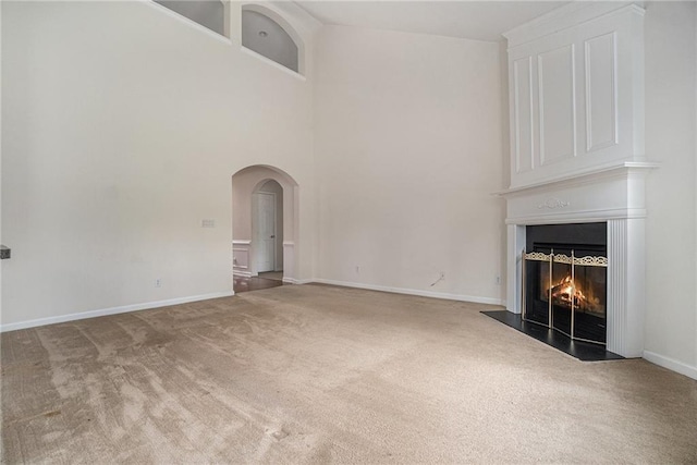 7761 Parkside Dr, Lithia Springs, GA 30122 - unfurnished living room with carpet floors, a large fireplace, arched walkways, a towering ceiling, and baseboards