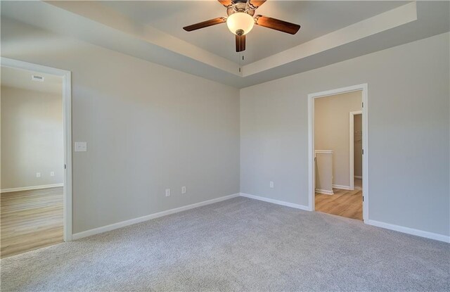 empty room with ceiling fan, light colored carpet, and a tray ceiling