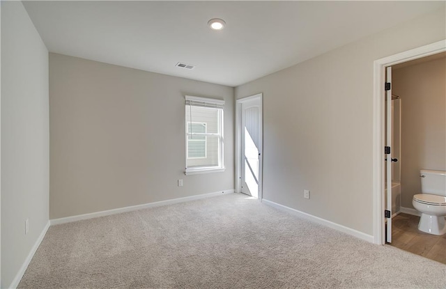 unfurnished bedroom featuring ensuite bathroom and light colored carpet