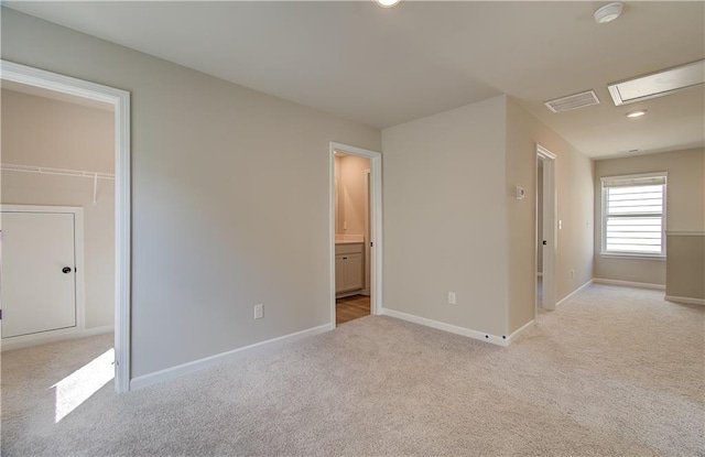 unfurnished bedroom featuring light colored carpet, a walk in closet, connected bathroom, and a closet