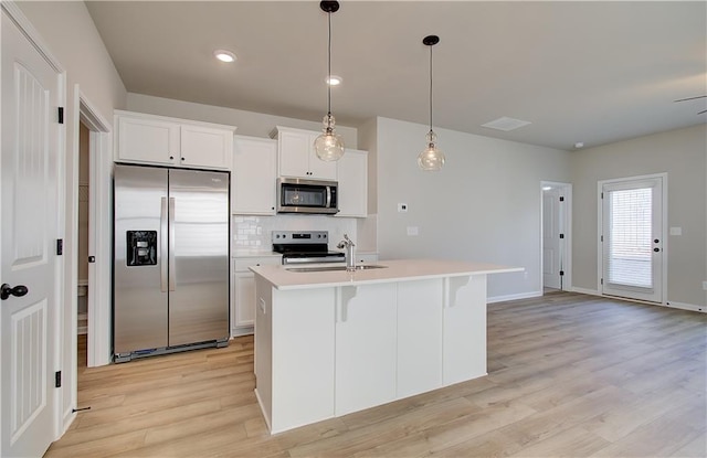 kitchen with white cabinetry, stainless steel appliances, pendant lighting, light hardwood / wood-style floors, and a center island with sink