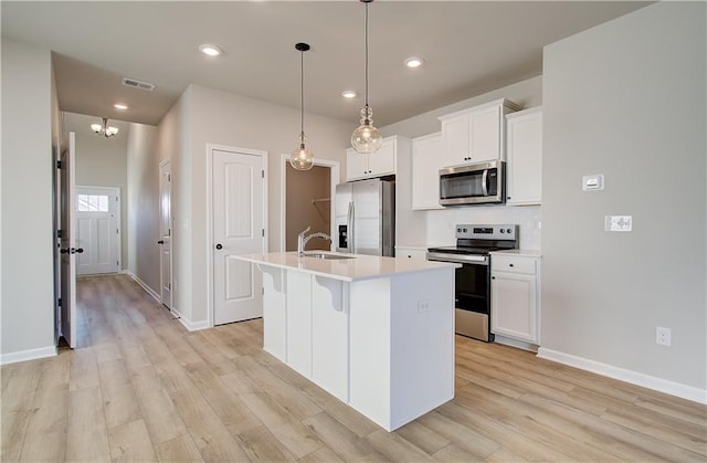 kitchen with a center island with sink, light hardwood / wood-style flooring, decorative light fixtures, white cabinetry, and stainless steel appliances