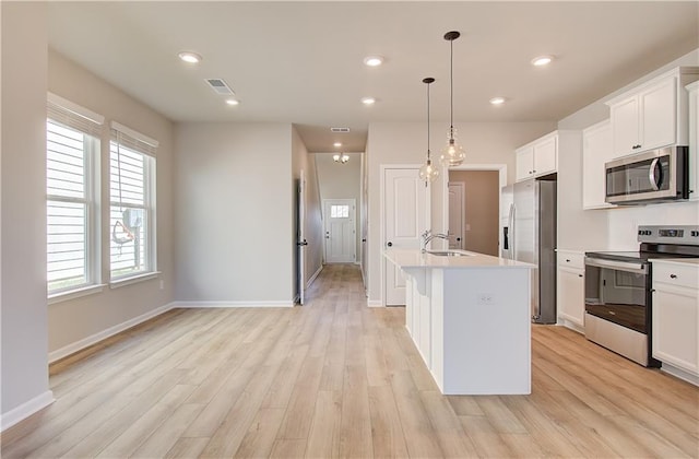 kitchen with hanging light fixtures, stainless steel appliances, a center island with sink, white cabinets, and light wood-type flooring