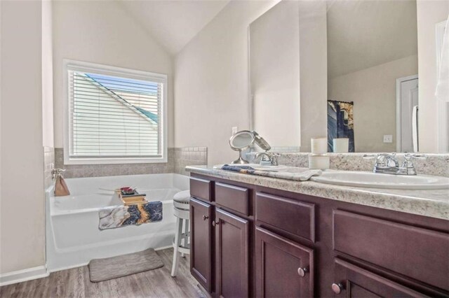 bathroom with hardwood / wood-style flooring, vanity, a bathtub, and vaulted ceiling