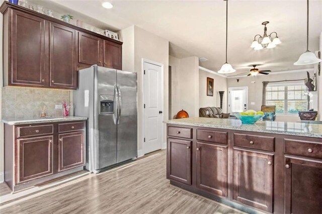 kitchen with ceiling fan with notable chandelier, light stone countertops, decorative light fixtures, light hardwood / wood-style floors, and stainless steel fridge with ice dispenser