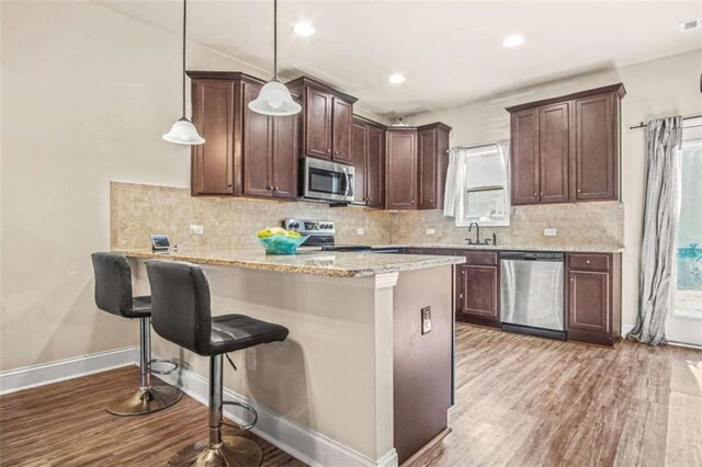 kitchen featuring kitchen peninsula, a breakfast bar, stainless steel appliances, decorative light fixtures, and light hardwood / wood-style flooring