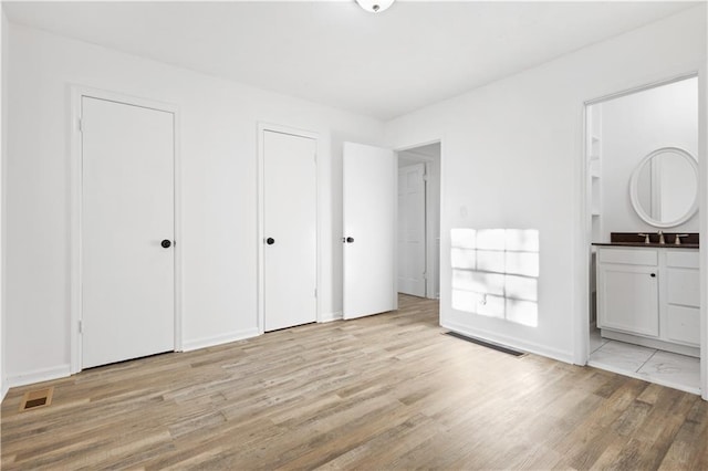 unfurnished bedroom featuring a sink, ensuite bath, light wood-style flooring, and multiple closets