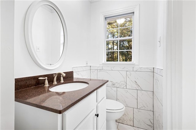 bathroom featuring toilet, a wainscoted wall, tile walls, and vanity