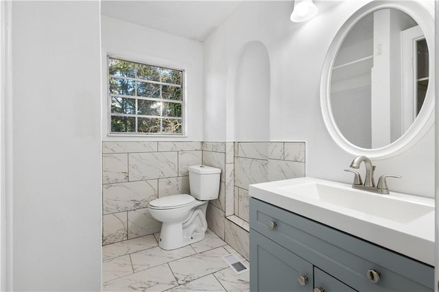 half bath with visible vents, toilet, a wainscoted wall, marble finish floor, and vanity