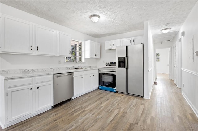 kitchen with stainless steel appliances, light wood-style floors, white cabinets, a sink, and a textured ceiling