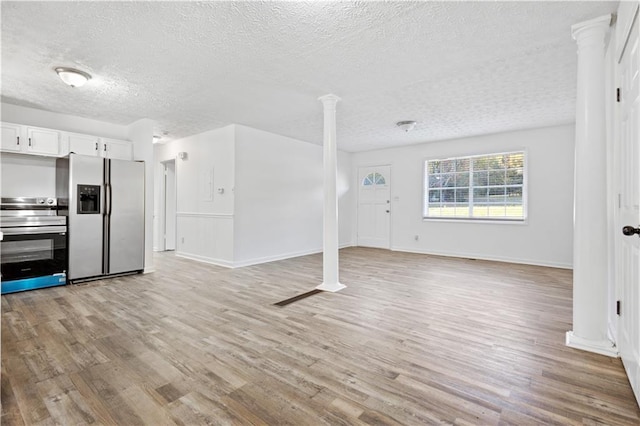 unfurnished living room with light wood-type flooring, ornate columns, baseboards, and a textured ceiling