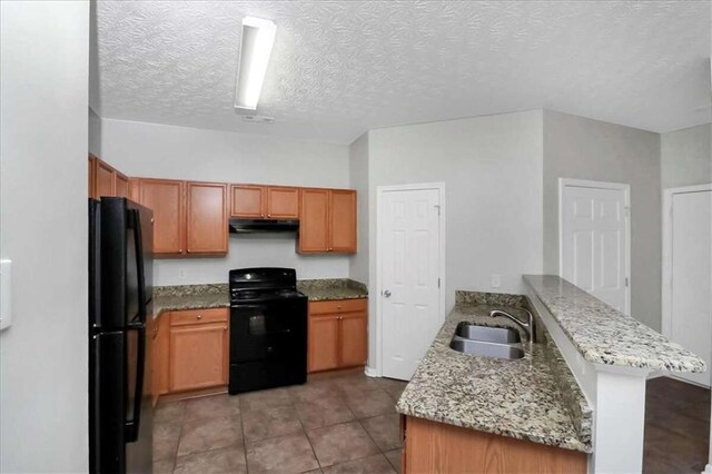 kitchen with light stone counters, sink, kitchen peninsula, a textured ceiling, and black appliances