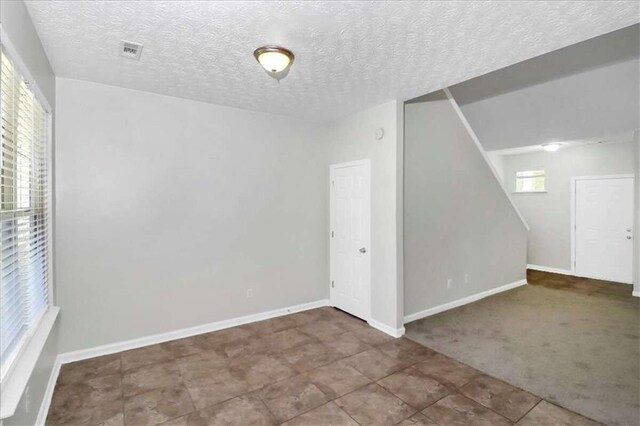 carpeted empty room featuring a textured ceiling and a healthy amount of sunlight