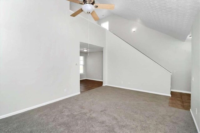 unfurnished living room featuring ceiling fan, a textured ceiling, lofted ceiling, and dark carpet