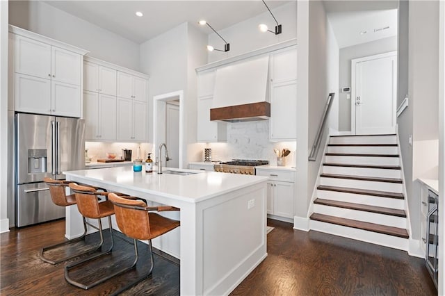 kitchen featuring premium range hood, an island with sink, a sink, light countertops, and appliances with stainless steel finishes