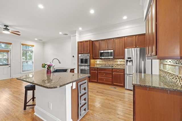 kitchen featuring sink, a kitchen island with sink, dark stone countertops, stainless steel appliances, and a kitchen breakfast bar