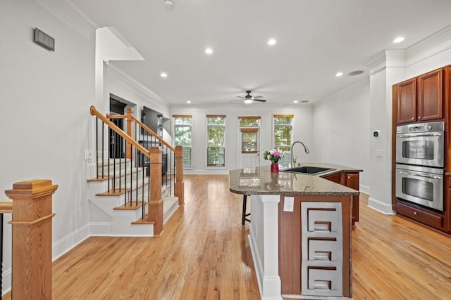 kitchen featuring dark stone countertops, crown molding, stainless steel double oven, and a center island with sink