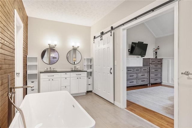 bathroom with a bathtub, vanity, a textured ceiling, vaulted ceiling, and hardwood / wood-style floors